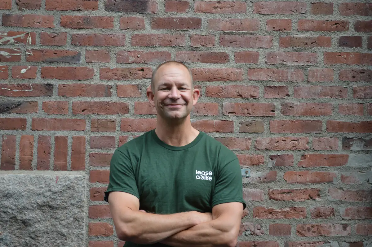 Man with Kalkhoff bike is standing in front of dark wall.